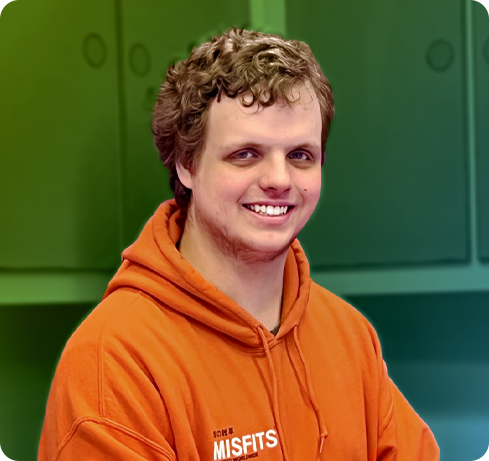 A picture of Max Lowe. He has blonde hair and blue eyes and is smiling happily with his arms crossed and posed for a photo. He is wearing a bright orange hoodie.